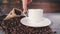 Coffee cup on gray marble table with coffee bag, coffee beans and cinamon. A hand enters and turns around the cup.