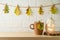 Coffee cup and jack o lantern pumpkin decoration on wooden shelf over brick wall background with autumn leaf garland. Halloween