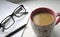 Coffee cup and a piece of paper with a writing pen and glasses on a light surface. Work. Read and edit the document.