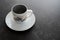 A coffee cup placed on a white saucer placed on a dark stone table with copy space