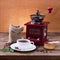 Coffee cup and saucer, coffee grinder, coffee beans in sack and spilled on wooden table.