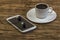 Coffee Cup on saucer, smartphone and earphones on wooden surface