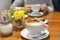 A coffee cup on a wooden table and a pair of woman`s hands holding another cup at the background