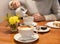 A coffee cup on a wooden table and a pair of woman`s hands holding another cup at the background