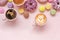 Coffee cups, delicious pink donuts with sprinkle and colorful bright macaroons on pink paper background