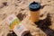 Coffee in a disposable cup and burger from Burger King lie on the sand under the sun