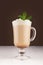 Coffee drink with cream and fresh green mint for breakfast in transparent glass with handle in dark brown interior on white wood.