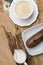 Coffee eclairs with cup of fresh black coffee on wooden table, chamomile flower. Top view.