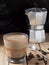 Coffee in a glass with cream and coffee beans on a wooden background. Near moka pot and spoon. Close up