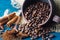 Coffee grains pouring out of a clay cup  and scattered on a blue textural background, anise stars, cinnamon sticks and ground