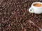 Coffee grains are scattered on a wooden table. A white cup with freshly brewed espresso stands in coffee beans. Wooden spoon.