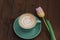 Coffee in a green cup with a pink tulip on a wooden background