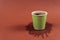 Coffee in green paper cup on brown background with stain. Spilled espresso on table. Glass with americano on coffee
