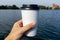 Coffee at the lake. Young woman holds a disposable cup of coffee on on a sunny day