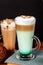 Coffee latte macchiato with mint syrup and whipped cream, in high transparent glasses with cakes, on a dark background