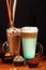 Coffee latte macchiato with mint syrup and whipped cream, in high transparent glasses with cakes, on a dark background