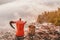 coffee maker and mug on a rock at the top of the mountain overlooking the misty dawn. Concept of tableware for camping and