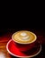 Coffee with milk foam froth art served in red cup on desk dark background with copyspace.