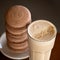 Coffee with milk and gourmet dessert. Close up shot of glass with frothy latte sprinkled with sesame seeds and stack of