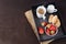 Coffee, mini French pastries and strawberries on wooden tray over black table. Black background
