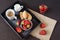 Coffee, mini French pastries and strawberries on wooden tray over black table. Black background