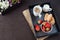 Coffee, mini French pastries and strawberries on wooden tray over black table. White and purple flowers in a decorative wooden