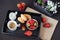 Coffee, mini French pastries and strawberries on wooden tray over black table. White and purple flowers in a decorative wooden