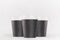 Coffee mockup - group of three blank black paper cups with white cap closeup on white wood table, coffee shop interior.