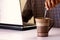 Coffee in a mug being stirred by a man working on a laptop computer in the background