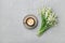 Coffee mug with bouquet of flowers lily of the valley on gray stone table from above in flat lay and minimalistic style.