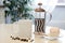 Coffee mug mockup in the kitchen interior. White ceramic cup on the table with a french press and some dessert