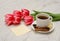 Coffee mug with spices, clean note, pink tulips on a wooden background, spring breakfast