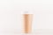 Coffee packing mockup - big kraft brown paper cup with white cap on white wood board, coffee shop interior.