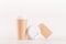 Coffee packing mockup - kraft brown paper cups, blank white cap and label on white wood board, coffee shop interior.