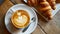 Coffee with a perfect latte art heart, next to a plate of fresh croissants