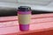 Coffee pink paper cup with black cap close-up on a red bench on a blurred background