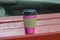 Coffee pink paper cup with a black lid on a red bench on a blurred background