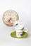 Coffee pot on a green saucer, decorative patterned clock and white daisy flower on a white background