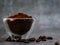 Coffee powder in glass bowl with beans scattered below