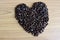 Coffee seeds pile heart symbol sign on wooden background closeup.