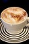 Coffee in a white cup on a striped saucer with a dark background.