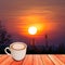 Coffee in white pottery cup on plank wood with sunrise