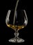Cognac is poured into a glass, a spray of a drink, on a black background