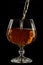 Cognac is poured into a glass, a spray of a drink, on a black background