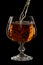 Cognac is poured into a glass, a spray of a drink, on a black background