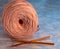 A coil of large knitted yarn of peach color with two orange shiny hooks on the surface of blue marble