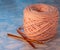 A coil of large knitted yarn of peach color with two orange shiny hooks on the surface of blue marble