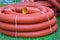 Coils of new red plastic pipe with rain drops on city lawn with green grass