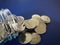 Coin money pouring out of glass bottle on blue background.