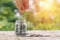 Coins in glass bottle put on table with hand putting money coins nature background.